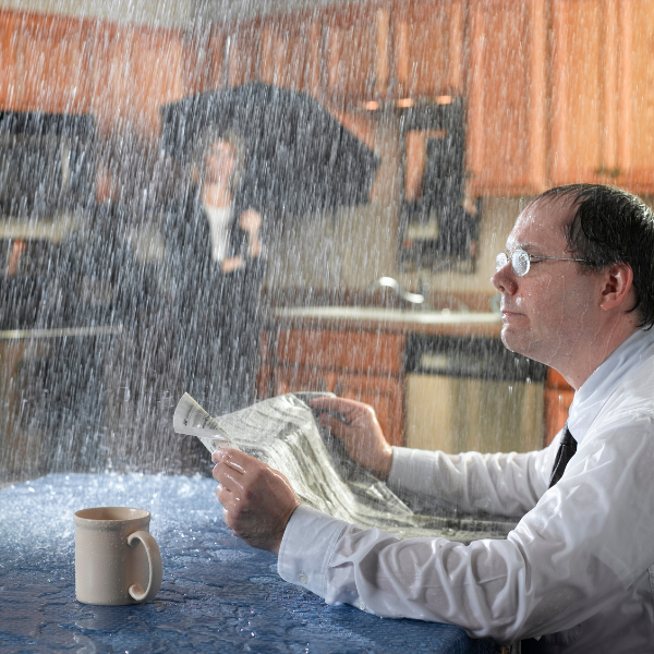 Roofing Welland - man reading the paper while rain is pouring inside the house